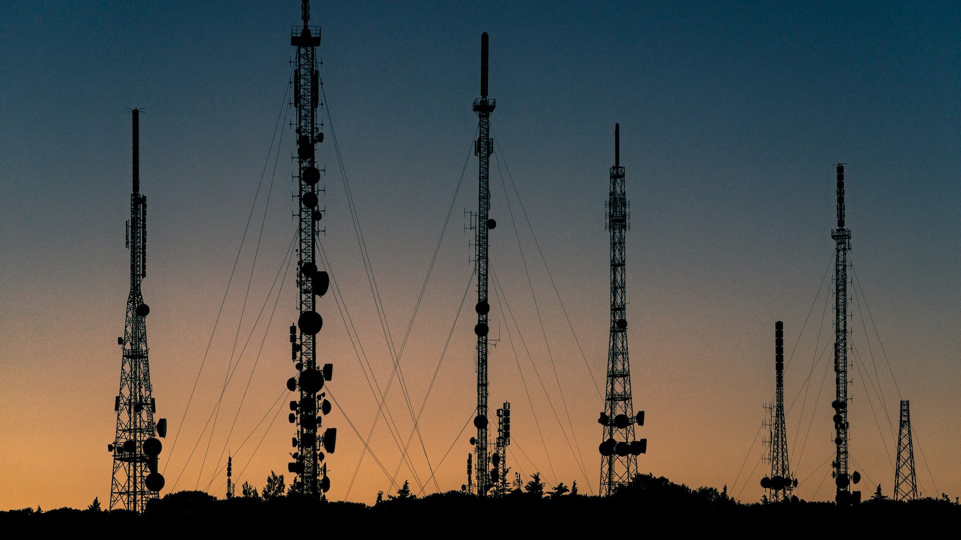 A landscape photo of several cellular towers set to the backdrop of sunset