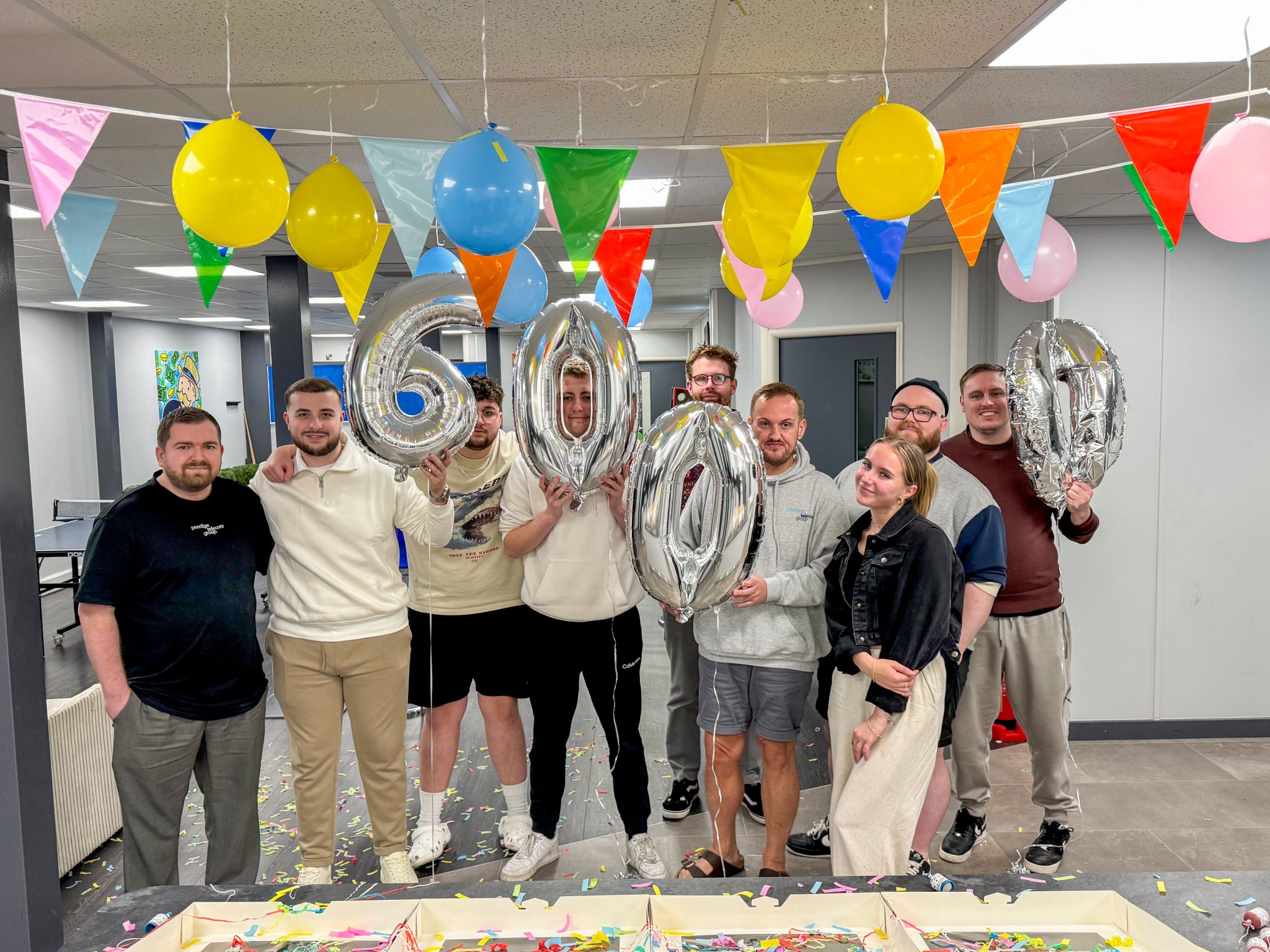 A group photo of the Prestige Telecom Group team, celebrating 6000 Trustpilot reviews with balloons that shape the number '6000'